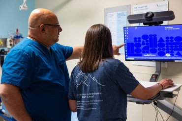 Lalit Bajaj points to a computer screen, standing beside fellow emergency physician Julia Fuzak Freeman.