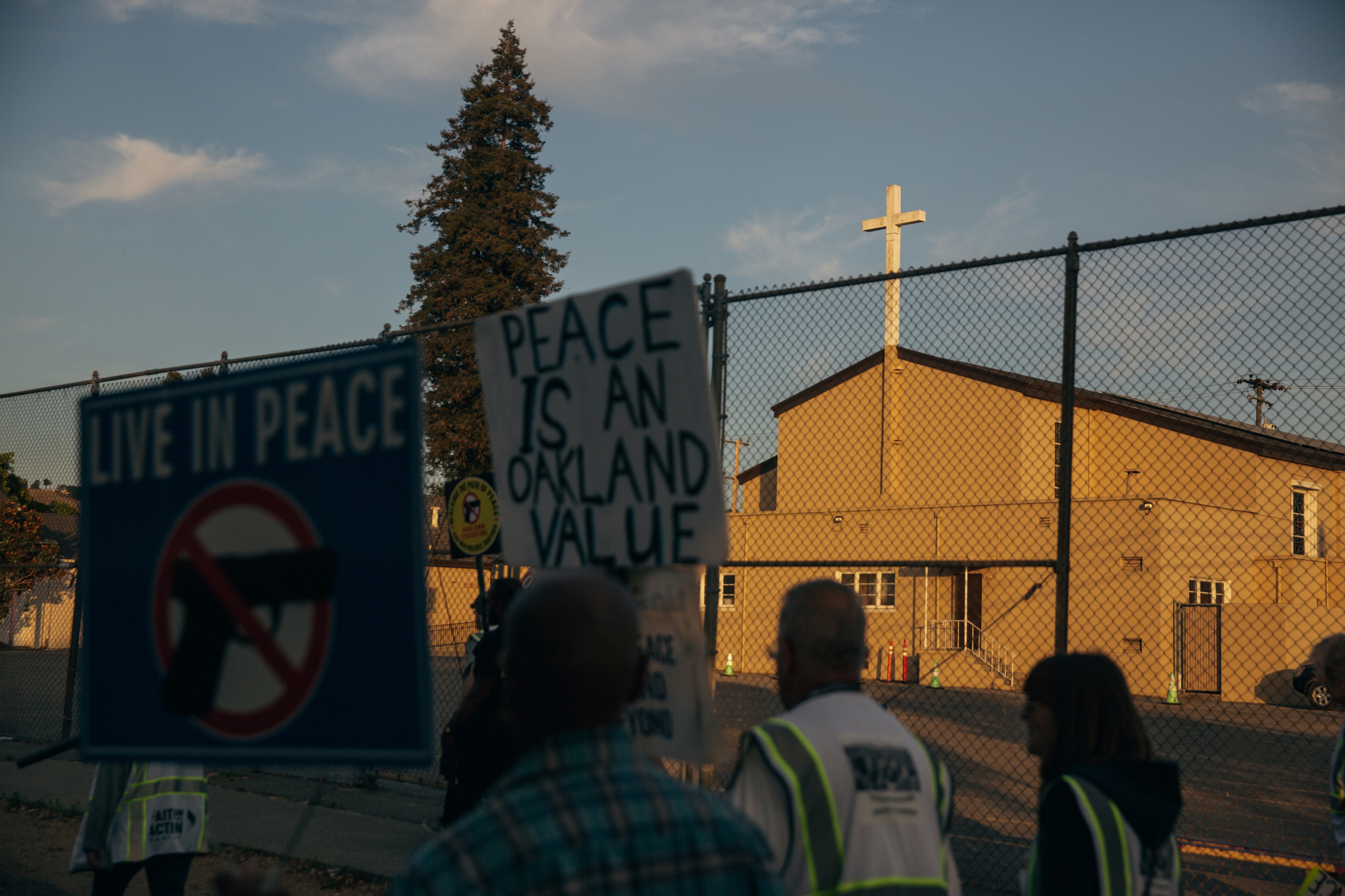 People walk past a church. Some wear reflective vests and some carry signs that read "Live in Peace" and "Peace is an Oakland value".